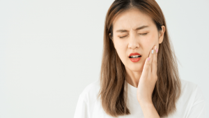 Clínica Dental Francos Rodríguez 28 Primer plano de perfil de una persona sosteniendo una muela del juicio recién extraída entre los dedos y señalando con la otra mano la zona de su mandíbula en Tetuán, Madrid.