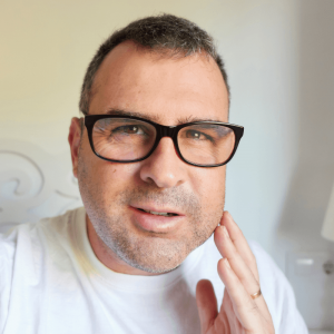 Primer plano de una persona con un bulto en la encía y la mejilla muy hinchada por un flemón dental, señalando con el dedo para indicar dolor e inflamación.